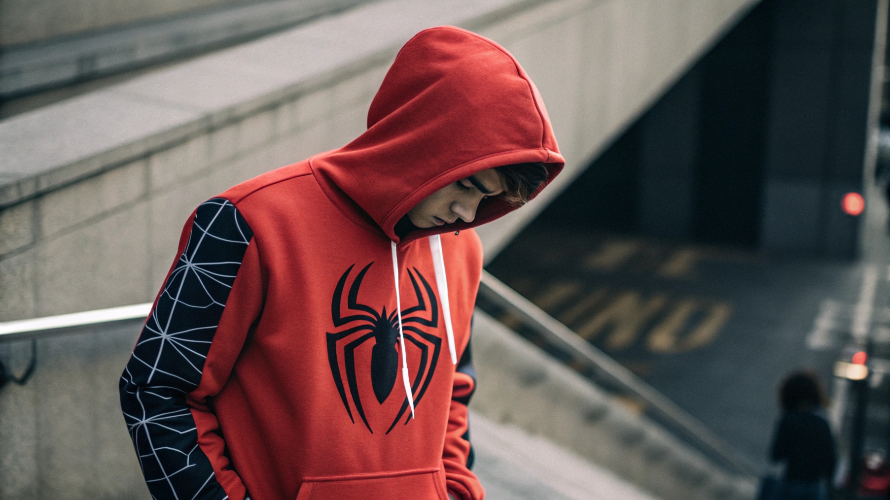 A person wearing a Sp5der hoodie with the iconic spider logo, styled in a trendy streetwear look. The background includes subtle references to social media platforms and hype culture, featuring social media posts and influencer style shots with the hoodie. A celebrity like Young Thug is subtly represented, emphasizing the role of celebrity endorsements in boosting the brand’s popularity. The scene highlights the hoodie’s street credibility and growing demand driven by social media and limited-edition releases