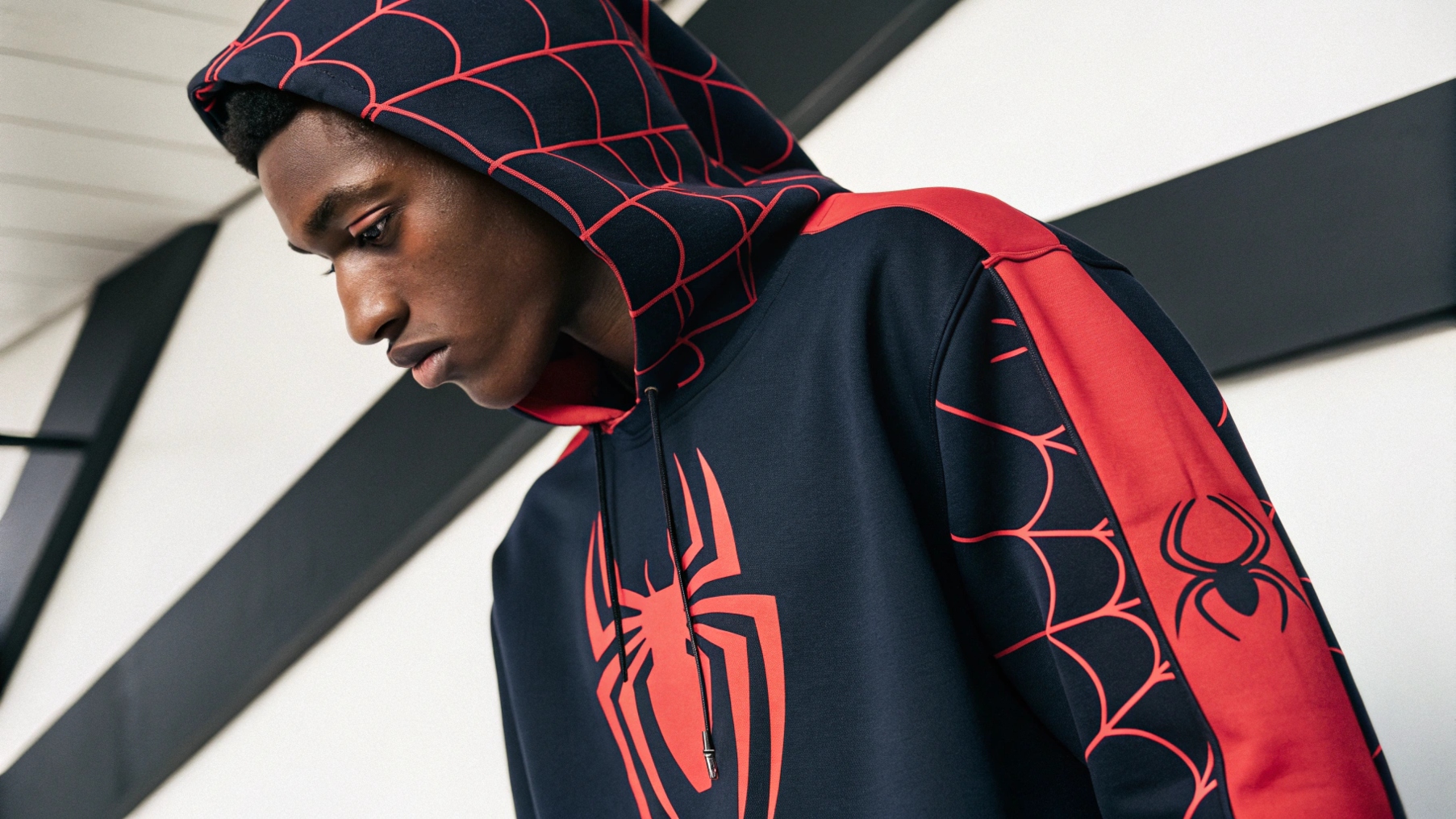  A person wearing a Sp5der hoodie with the iconic spider logo and bold graphic design, showcasing the hoodie as a statement piece in luxury streetwear. The vibrant colors and striking prints make it stand out, while the soft cotton blends and fleece highlight the high-quality materials. The scene emphasizes attention to stitching and craftsmanship, with a minimal background drawing focus to the unique design and premium quality of the Sp5der hoodie.